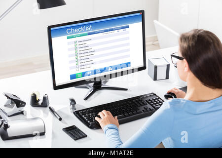 Nahaufnahme einer Geschäftsfrau Füllung Checkliste Formular auf dem Computer am Schreibtisch aus Holz Stockfoto