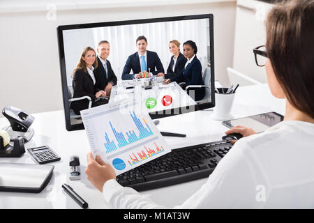 Frau diskutieren Graph mit Ihren Kollegen auf Video Konferenz am Computer am Arbeitsplatz Stockfoto