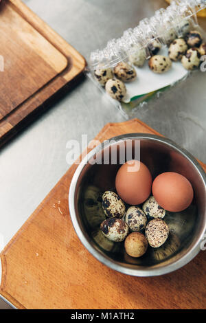 Blick von oben auf die Hühnchen und Wachteleier in Metall Schüssel am Küche Stockfoto