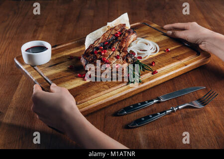 Schuß von Frau mit gegrilltes Steak mit Sauce und Granatapfel Samen auf Holzbrett serviert 7/8 Stockfoto