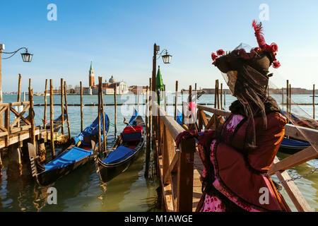 Unbekannter Teilnehmer im Kostüm steht in der Nähe von Gondeln am Canale Grande gekleidet, wie die Kirche San Giorgio Maggiore in Venedig auf Hintergrund. Stockfoto