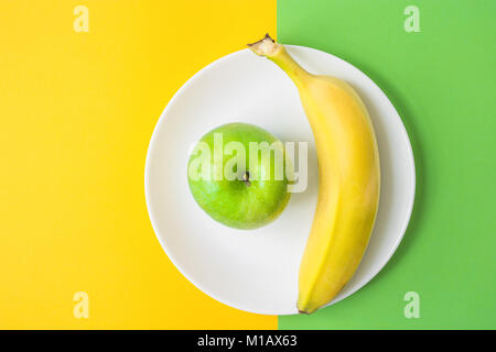 Grüner Apfel Banane auf weiße Platte auf Kontrast Hintergrund von der Kombination von gelben und grünen Farben. Vitamine gesunde Ernährung Frühling Sommer Detox Vegan. Stockfoto