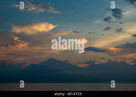 Ein Blick aus dem Ozean der Vulkan Mount Rinjani auf der Insel Lombok, Indonesien bei Sonnenuntergang, mit blauem Himmel und Goldene Wolken über, und das Meer unten. Stockfoto