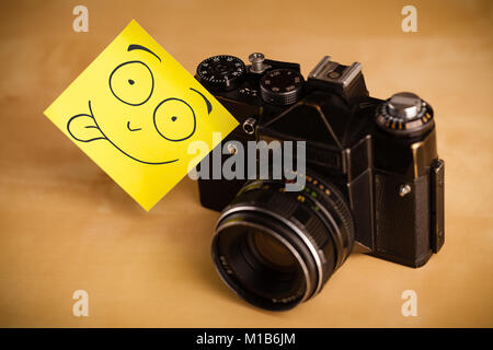 Gezeichnet Smiley auf einem Post-it Note aufgeklebt auf einem alten Foto Kamera Stockfoto
