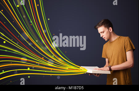 Junger Mann, ein Buch zu lesen, während bunte Zeilen aus dem Buch kommen Stockfoto