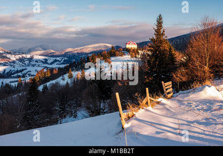 Synevyr, Ukraine - Jan 19, 2016: Auf dem Land in den Karpaten bei Sonnenaufgang. schöne Landschaft mit hölzernen Zaun und Nadelwald auf einem schneebedeckten Slo Stockfoto