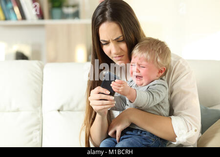 Baby in einen Wutanfall und kämpfe mit seiner Mutter für ein smart phone auf einer Couch im Wohnzimmer zu Hause sitzen Stockfoto