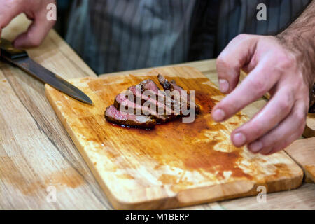 Koch Hände schneiden Steaks mit Messer auf Schneidebrett. Warme Gerichte Konzept Stockfoto