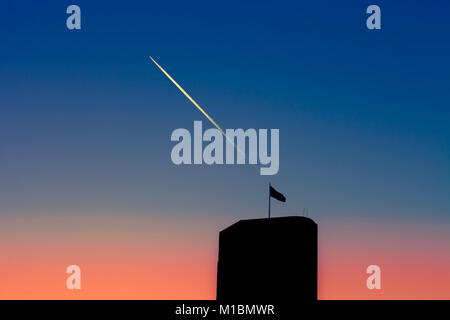 Silhouette der Wolkenkratzer mit Flagge gegen einen Farbverlauf Himmel mit turbojet Trails oben Stockfoto