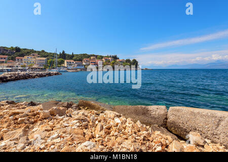 An der felsigen Küste des Ionischen Meeres und Häuser auf dem Hügel in der Ferne. Kassiopi Village auf Korfu. Griechenland Stockfoto