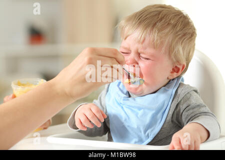 Nahaufnahme der Mutter Hand Feeding seinen Sohn, der weinend sitzt auf einem hohen Stuhl Stockfoto