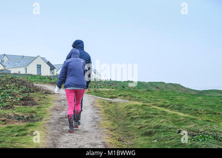 De Winter Wetter - Menschen paar Wanderer Wandern auf dem South West Coast Path während der kalten winterlichen Wetterbedingungen. Stockfoto