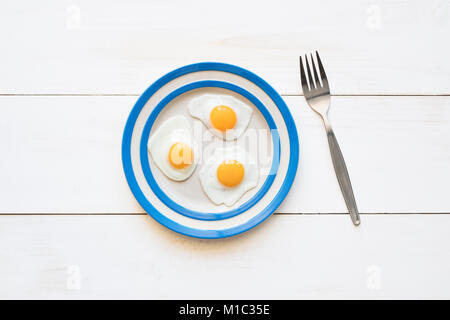 Gebratene Wachtel Eier auf einem cornishware Platte mit einer Gabel von oben Stockfoto