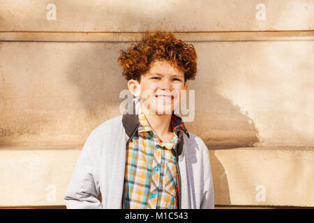 Close-up Portrait von Teenage curly schwarzhaarige Junge stehend gegen die Wand an einem sonnigen Tag und Blick auf die Kamera Stockfoto