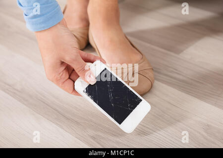 Nahaufnahme einer Frau, die Kommissionierung, die Gebrochenen Smart Phone aus Hartholz Stock Stockfoto