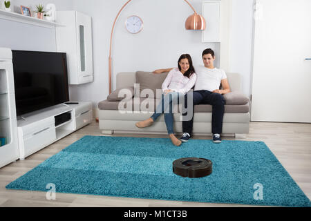 Lächelnde junge Paar sitzt auf dem Sofa anschauen Reinigungsroboter Stockfoto