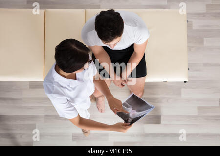 Junge Ärztin, die Knie X-ray Zu männlichen Patienten Stockfoto