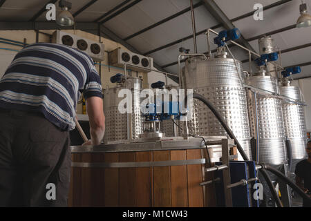 Ansicht der Rückseite des männlichen Arbeitnehmers rühren Gin in der Brennerei im Werk Stockfoto