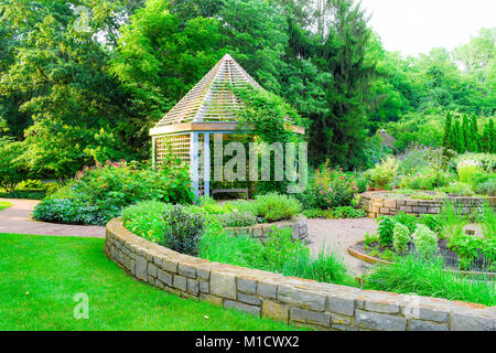 Ein straßenfertiger Pfad führt durch einen üppigen Garten, der vergeht, ein Pavillon im Licht wie die Sonne sinkt. Stockfoto