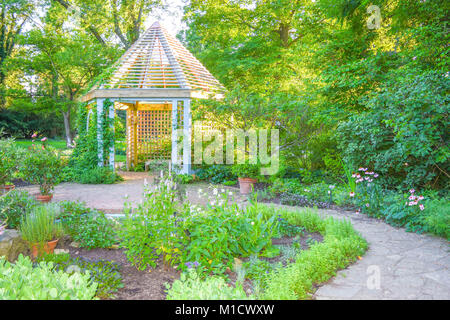 Ein Stein Trail, der durch einen schönen Garten führt zu einer gelassenen Pavillon in den Sonnenuntergang. Üppige Bäume und Evergreens umgeben die wunderschöne Lage. Stockfoto