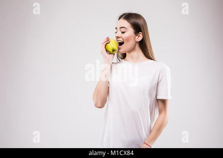 Closeup Portrait schöne junge Brünette Frau beißen saftigen frischen köstlichen Apfel vor grauem Hintergrund. Schöne junge Dame, die gesunde Ernährung. Stockfoto