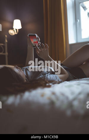 Frau mit Handy im Schlafzimmer Stockfoto
