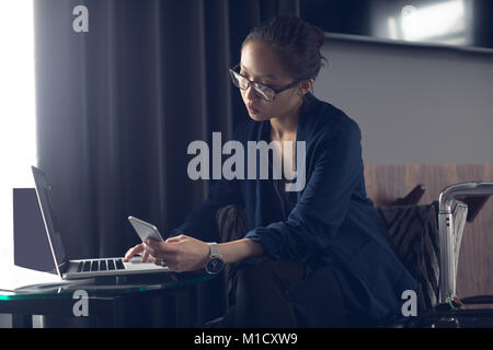 Frau mit Handy und Laptop am Tisch Stockfoto