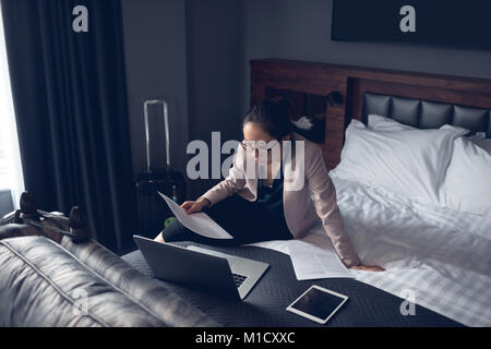 Frau liest Dokument während der Arbeit am Laptop Stockfoto