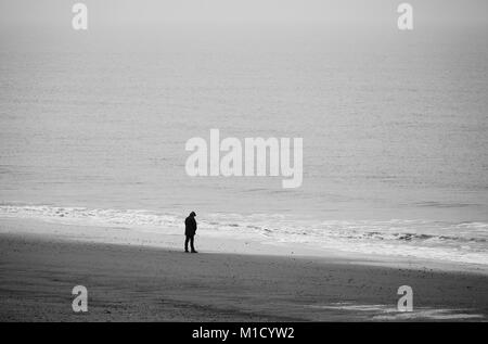 Ein Mann, der allein an einem Strand mit Blick auf das Meer. Stockfoto