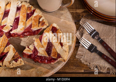 Blick von oben auf ein Cherry Pie mit einem Stück heraus auf eine hölzerne Platte geschnitten Stockfoto
