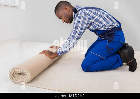 Junge männliche Heimwerker Rolling Teppich auf dem Boden zu Hause Stockfoto