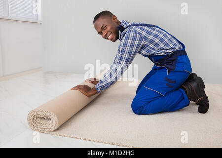 Junge männliche Heimwerker Rolling Teppich auf dem Boden zu Hause Stockfoto