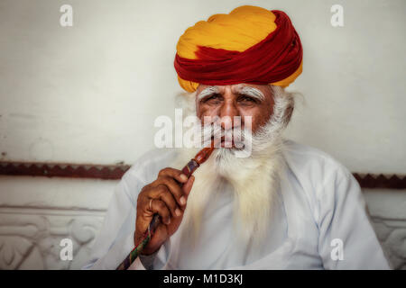Alter Mann in traditionellen Rajasthani Kleid und bunten turban Rauchen einer Wasserpfeife an Mehrangarh Fort. Stockfoto