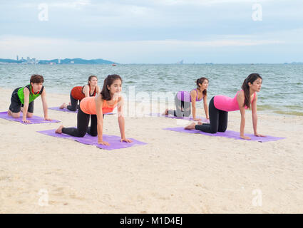 Yoga am Meer Strand im Sonnenuntergang am Abend, einer Gruppe von Menschen, die Katze wirft mit Clam emotion am Strand entspannen, Meditation, Wellness und gesunden Balan Stockfoto