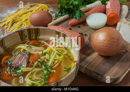 Hühnersuppe in einem rustikalen Schüssel und Zutaten auf hölzernen Tisch Stockfoto