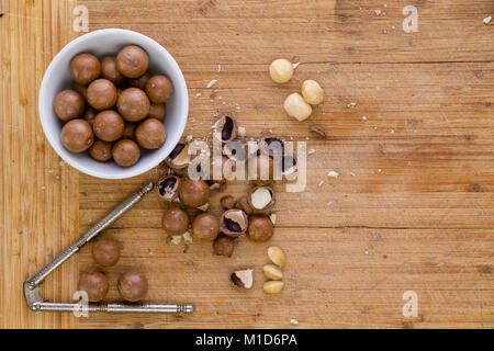 Beschuss frischen Macadamia Nüsse für Essen oder Kochen in einer Ansicht von oben bei ganzen Nüssen, geknackte Muscheln und ein Nussknacker auf Holz Bambus board mit c Stockfoto