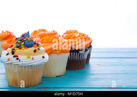 Drei verschiedene iced Cupcakes in einem rückläufigen Zeile mit Schokolade und Vanille cookies mit Orangenglasur und Vordergrund Kuchen mit weißer Zuckerglasur autolöscher Stockfoto