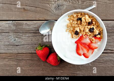 Schüssel mit Joghurt mit Erdbeeren und Müsli über eine rustikale Holz Hintergrund. Flach. Stockfoto