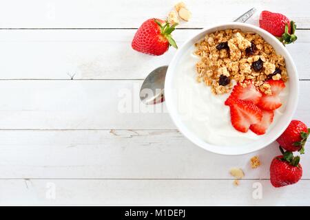Schüssel mit Joghurt mit Erdbeeren und Müsli, über einem weißen Holz Hintergrund. Flach, seitliche Ausrichtung. Stockfoto