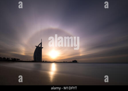 Skyline von Dubai bei einem farbenfrohen Sonnenuntergang mit einem seltenen Sun halo wie vom öffentlichen Strand gesehen. Dubai, VAE. Stockfoto