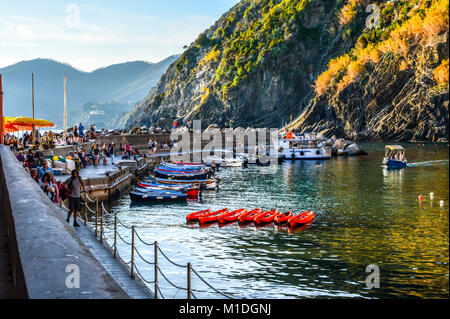 Die untergehende Sonne am späten Nachmittag am Hafen des Fischerdorfes Vernazza Cinque Terre Italien, mit Booten in das Meer und Touristen im Cafe Stockfoto