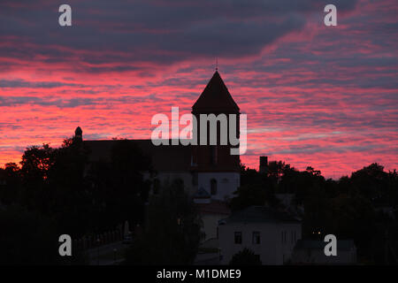 Mir, Belarus. Saint Nicolas Römisch-katholische Kirche in der Hintergrundbeleuchtung von erstaunlichen Sonnenuntergang über der Landschaft der Häuser des Dorfes. Das Wahrzeichen der Stadt. Historische Architektur Stockfoto