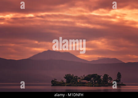 Kleines Haus auf der kleinen Insel inmitten des atemberaubenden Lake Maninjao bei Sonnenuntergang, Insel Sumatra, Indonesien Stockfoto