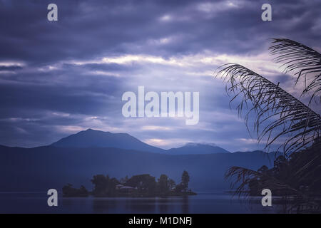 Kleines Haus auf der kleinen Insel inmitten des atemberaubenden Lake Maninjao bei Sonnenuntergang, Insel Sumatra, Indonesien Stockfoto