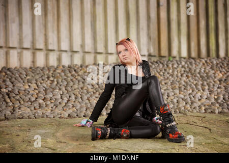 Hübsches Mädchen in der Stadt liegt, trägt einen schwarzen Outfit und Stiefel Stockfoto