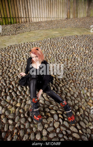 Hübsches Mädchen in der Stadt liegt, trägt einen schwarzen Outfit und Stiefel Stockfoto