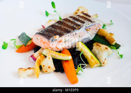 Lachs serviert auf schwarzer Reis mit Zucchini, Karotten und Blumenkohl. Stockfoto