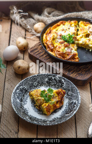 Ein Stück französische Omelette gebacken Savoy mit Schinken, Käse, Kartoffeln und Lauch auf einer Platte, rustikaler Stil, Ansicht von oben Stockfoto