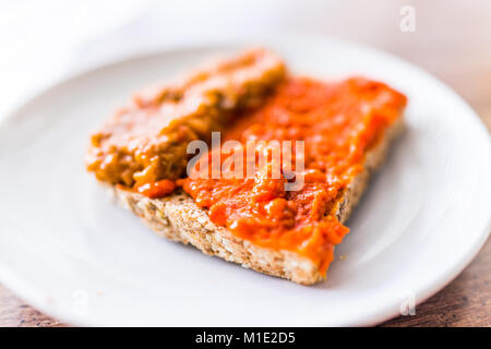 Nahaufnahme von slice Stück ganze Saat aufsproßte geröstetes Brot auf dem Teller mit orange red Paprika Gemüse Auberginen verteilen sich auf Tabelle Makro Stockfoto