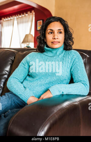 Ein Porträt eines Anfang 30 Sri Lanken - amerikanische Frau sitzt in ihrem Haus auf einem Ledersofa. Stockfoto